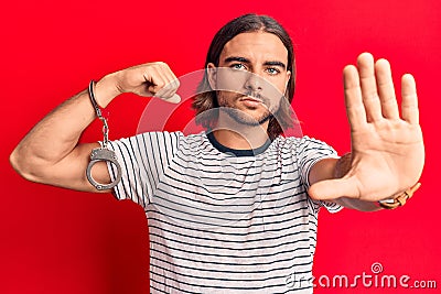 Young handsome man wearing prisoner handcuffs with open hand doing stop sign with serious and confident expression, defense Stock Photo