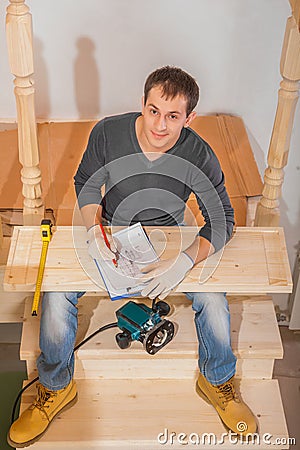 A young handsome man wearing working clothes sitting on ladder Stock Photo