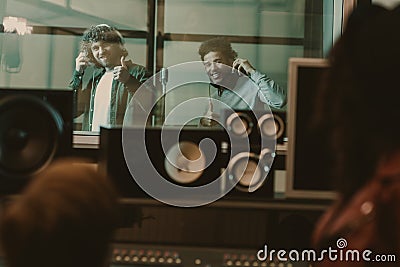 young handsome musicians recording song behind glass at studio and showing Stock Photo