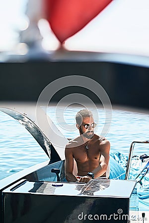 Tanned young handsome bearded muslim captain or skipper steering at the helm and control panel of a yacht under the red Stock Photo