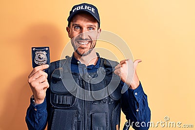 Young handsome policeman wearing uniform and bulletprof holding police badge pointing thumb up to the side smiling happy with open Stock Photo