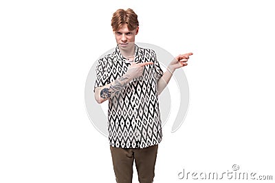 young handsome red-haired man dressed in a summer shirt with a rhombus print points his hand to the side Stock Photo