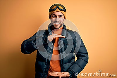 Young handsome skier man with beard wearing snow sportswear and ski goggles gesturing with hands showing big and large size sign, Stock Photo