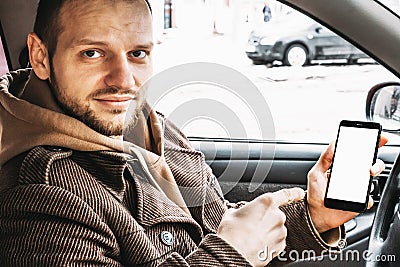 Young handsome smiling man showing smartphone or cellphone white screen as mock up for your product sitting in car Stock Photo