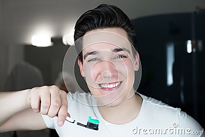 Young handsome smiling man with toothbrush in his hand brushing teeth in bathroom in the morning looking happy everyday routine Stock Photo