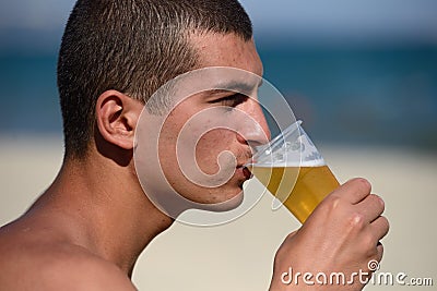 Young handsome sporty man drinking beer at the beach in summertime - relaxing, summer, thirsty concept. Resort relaxation. Sea in Stock Photo