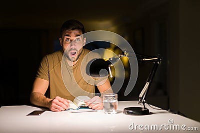 Young handsome student man studying at night at home scared in shock with a surprise face, afraid and excited with fear expression Stock Photo