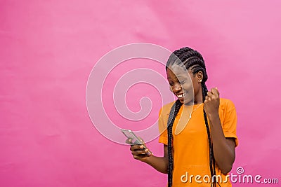 Young happy African-American female holding a cellular phone isolated on light pink background Stock Photo