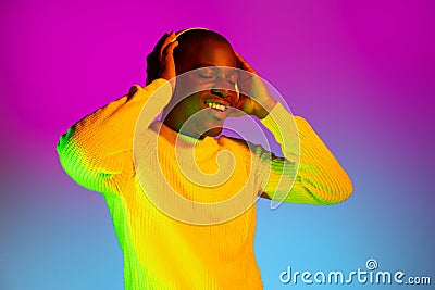 Young happy African handsome man with headphones isolated over gradient magenta yellow neon background. Stock Photo