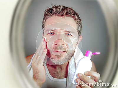 Young happy and attractive man applying moisturizer lotion or anti aging beauty cream smiling confident and conscious looking at b Stock Photo