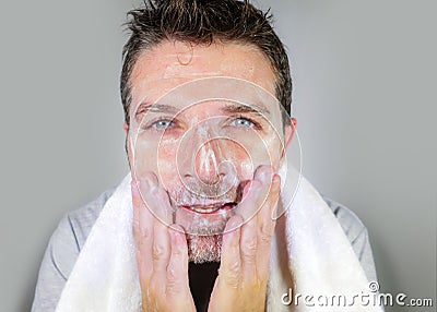 Young happy and attractive man washing face with anti aging soap lotion smiling confident and conscious looking at bathroom mirror Stock Photo