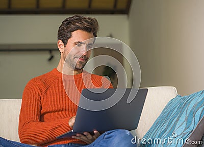 Young happy and attractive man working relaxed with laptop computer at modern apartment living room sitting at sofa couch typing a Stock Photo