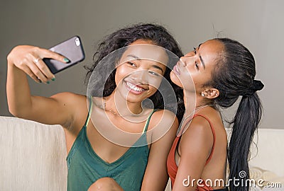 Young happy and beautiful Asian sisters or girlfriends couple smiling cheerful taking selfie photo with mobile phone at home Stock Photo