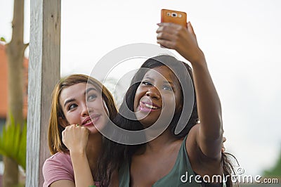 Young happy and beautiful black afro American woman enjoying holidays at tropical resort with Asian girlfriend taking selfie Stock Photo