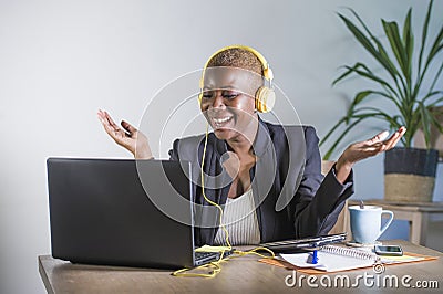 Young happy black afro american woman listening to music with headphones excited and joyful working at laptop computer desk at mod Stock Photo