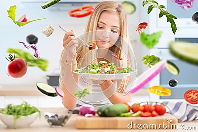 Young happy blonde girl eating healthy salad from arugula spinach tomatoes olives onion and olive oil. Healthy vegetable concept Stock Photo