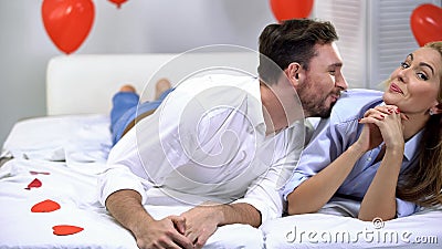 Young happy couple lying on bed and smiling to camera, man trying to kiss lady Stock Photo