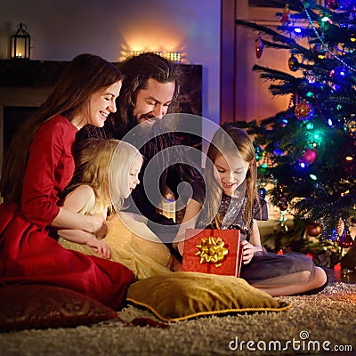 Young happy family of four unwrapping Christmas gifts by a fireplace Stock Photo