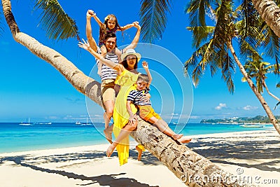 Young happy family-mom, dad, daughter and son having fun on a coconut tree on a sandy tropical beach. The concept of travel and Stock Photo