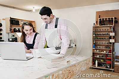 Young happy family standing at a work bench in a carpentry workshop, writing a project. Family business. startup business. young Stock Photo