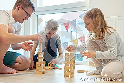 Young happy father playing with his two cute children with wooden blocks Stock Photo