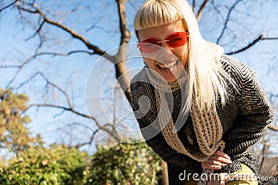 Young happy funny hippie girl showing tongue at camera for fun and making funny faces while wearing cool sunglasses. Attractive Stock Photo