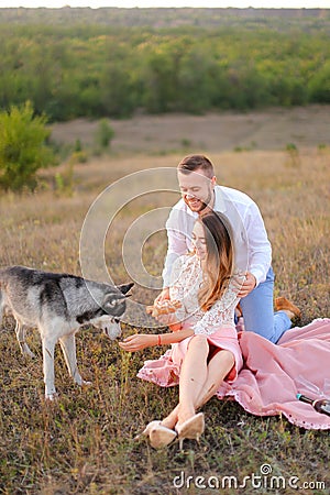 Young happy girl and boy sitting on pink plaid near husky and resting. Stock Photo