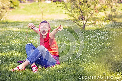 Young happy girl with earphones and smartphone listening to music on grass. Stock Photo