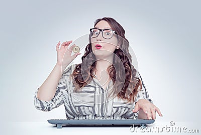 Young happy girl with glasses at the computer holds in her hand bitcoin. Digital money concept Stock Photo