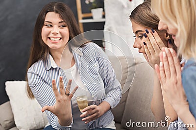 Young happy girl showing her proposal ring to surprised girlfriends Stock Photo