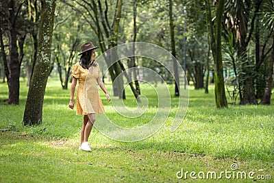 Young happy Hispanic woman walking through the park wearing a yellow dress and hat Stock Photo