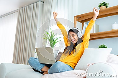 Young happy lucky woman student feeling excited winning, using computer laptop and sitting on sofa Stock Photo
