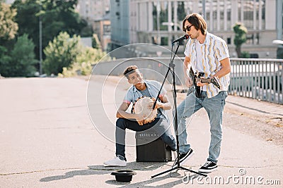 Young and happy male street musicians playing guitar and djembe Stock Photo