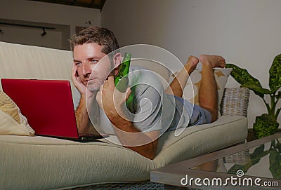 Young happy man lying at home sofa couch relaxed using internet on laptop computer watching online movie or working as independent Stock Photo