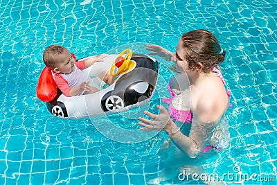 Young happy mother in a pink bikini having fun and catch baby in the pool. A joyful little child sits in an inflatable boat in the Stock Photo