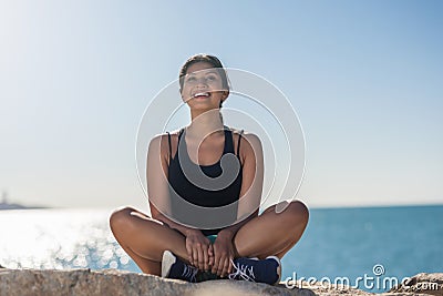 Young happy sportswoman sitting on rock at seaside Stock Photo