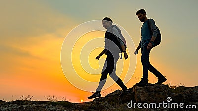 Young Happy Travelers Hiking with Backpacks on the Rocky Trail at Summer Sunset. Family Travel and Adventure Concept. Stock Photo