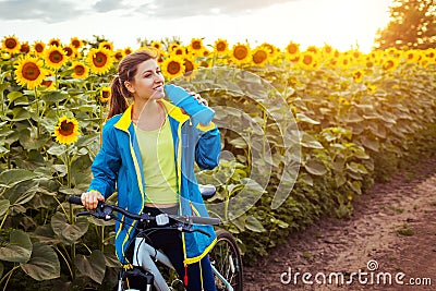 Young happy woman bicyclist drinking water after riding bicycle in sunflower field. Summer sport bike activity Stock Photo