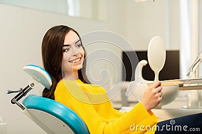 Young happy woman client looking at the mirror with toothy smile at the dental office Stock Photo