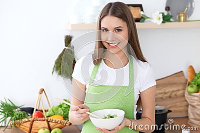 Young happy woman is cooking or eating fresh salad in the kitchen. Food and health concept Stock Photo