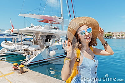 Happy woman in hat with backpack standing near sea port with luxury yachts. Travel and vacation concept Stock Photo