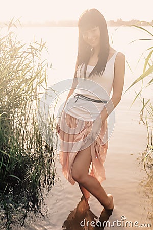 Young happy woman in nature lake view with reeds standing in lightfall of sunset Stock Photo