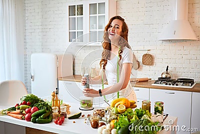 Young happy woman preparing tasty salad in the beautiful kitchen with green fresh ingredients indoors. Healthy food and Dieting Stock Photo
