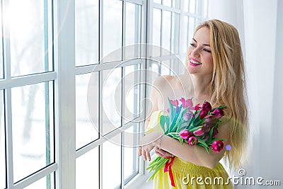 Young happy woman smiling with tulip bunch in yellow dress. 8 march international womens day. Stock Photo