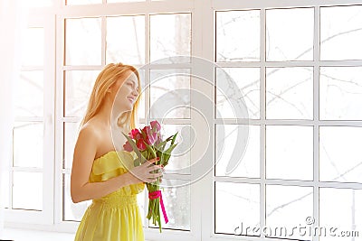 Young happy woman smiling with tulip bunch in yellow dress Stock Photo