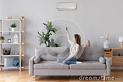 Young woman switching on air conditioner sitting on couch Stock Photo