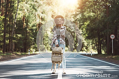 Young happy woman with traveling backpack wearing hat stand alone on countryroad Stock Photo