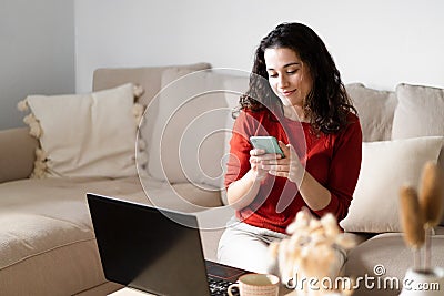 Young happy woman using the phone and the computer sitting on the couch Stock Photo