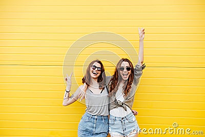 Young happy women friends standing over yellow wall Stock Photo