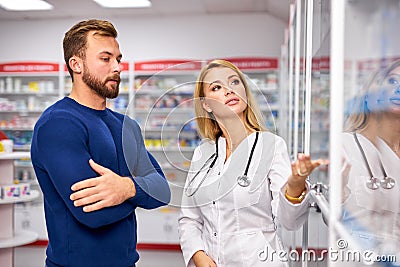 Young helpful female druggist dealing with a male customer, explaining a prescription Stock Photo